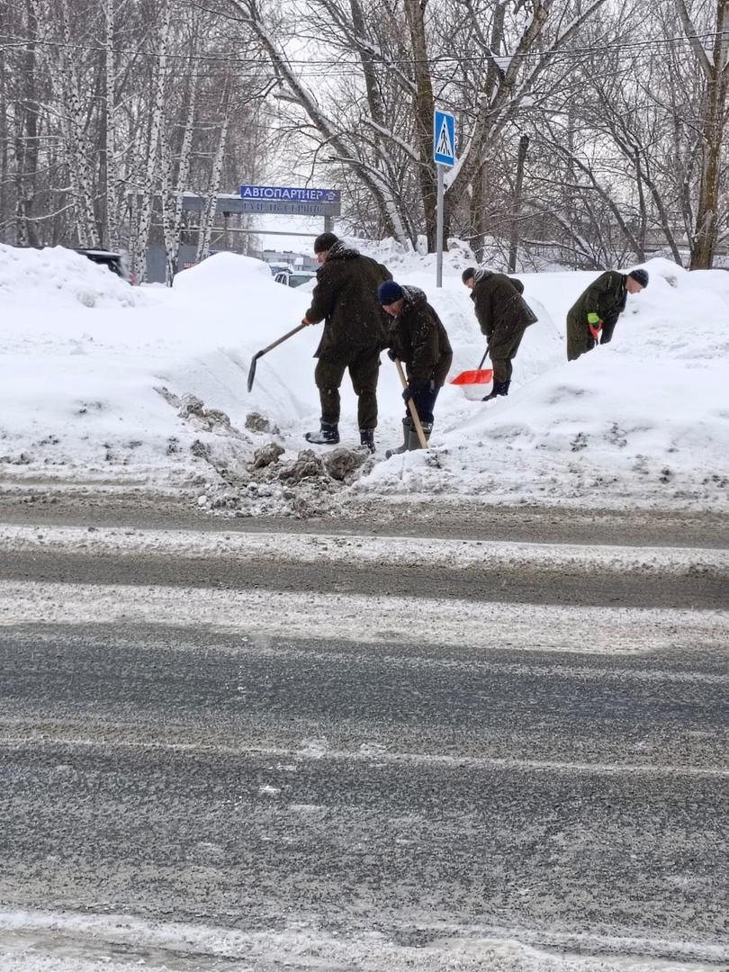 Сотрудники Управления гражданской защиты расчищают от снега автобусную остановку.