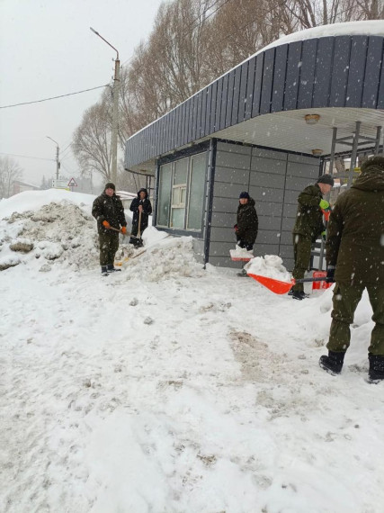 Сотрудники Управления гражданской защиты расчищают от снега автобусную остановку.